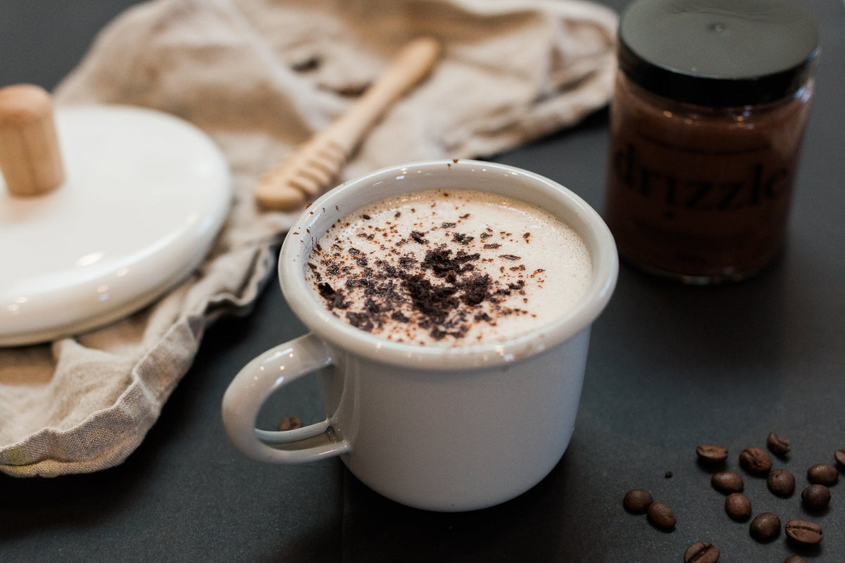Photo of Drizzle Cacao Luxe Honey next to a steaming cup of hot cacao in a kitchen.