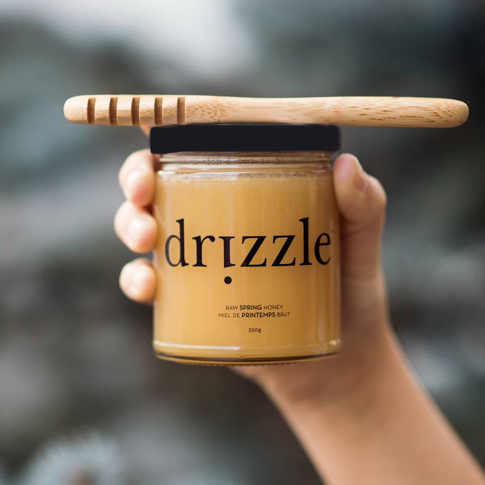 Drizzle Golden Raw Honey being held with a honey dripper on top.