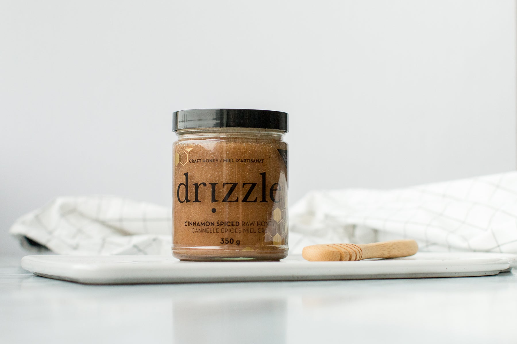 Drizzle Cinnamon Spiced Raw Honey in a white kitchen setting next to a drizzle spoon.