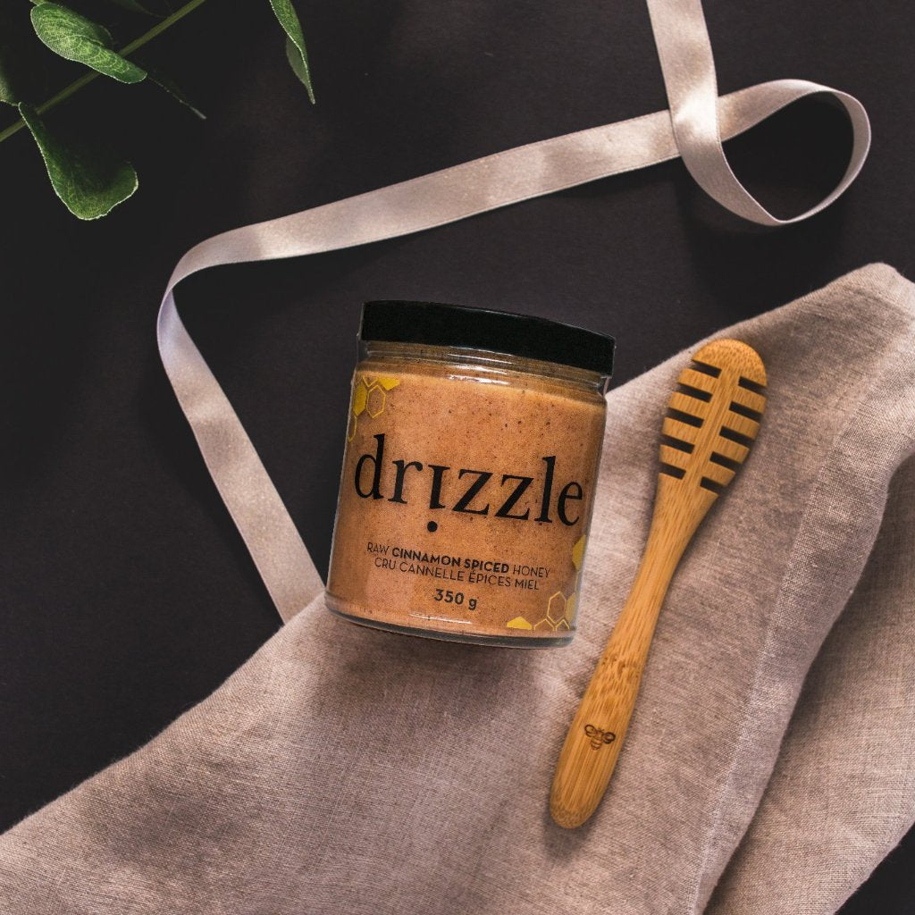 Drizzle Cinnamon Spiced Raw Honey next to a Drizzle Honey spoon with a beautiful cloth underneath.