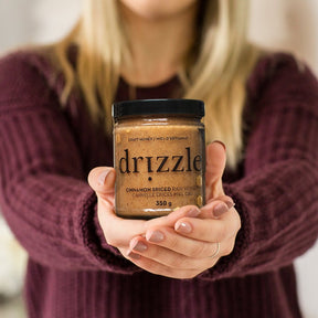 Drizzle Cinnamon Spiced Raw Honey being held outwards by a woman in a red sweater.