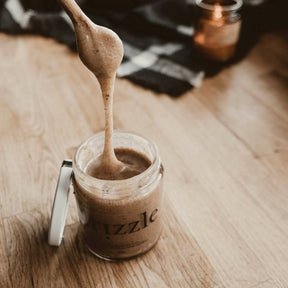Drizzle Cinnamon Spiced Raw Honey being drizzled into the jar with a spoon.