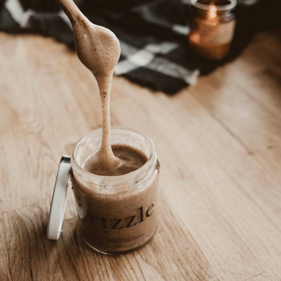 Drizzle Cinnamon Spiced Raw Honey being drizzled into the jar with a spoon.